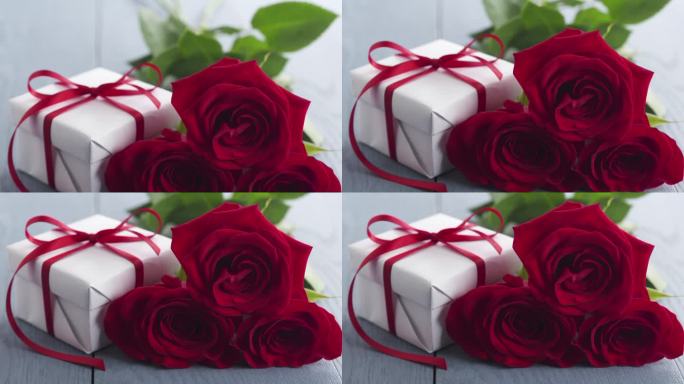 三朵红玫瑰和礼盒放在蓝色的木桌盘上
