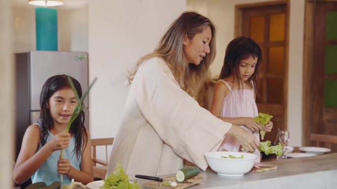 妇女和儿童在家庭厨房烹饪食物的幸福家庭。亚洲人和小孩用盘子准备素食餐。迷人的母亲和女孩在室内制作周末