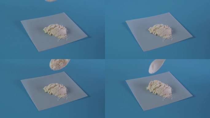 测量瓜尔胶粉的塑料勺子和蓝色表面的纸样品。食品添加剂E412。瓜尔胶常用于食品工业和化妆品，用于皮肤