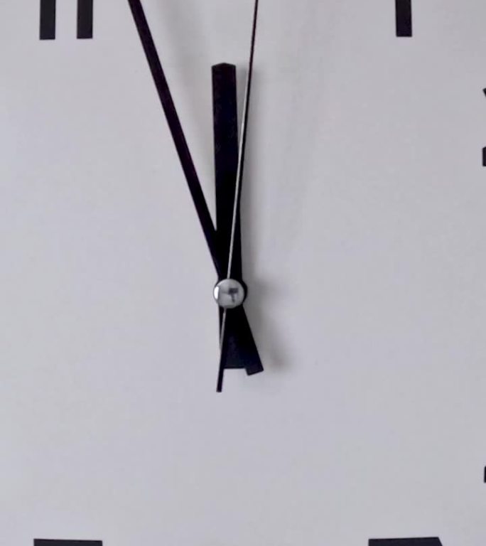 白色挂钟上的白色钟面特写，箭头显示11:55到12:00