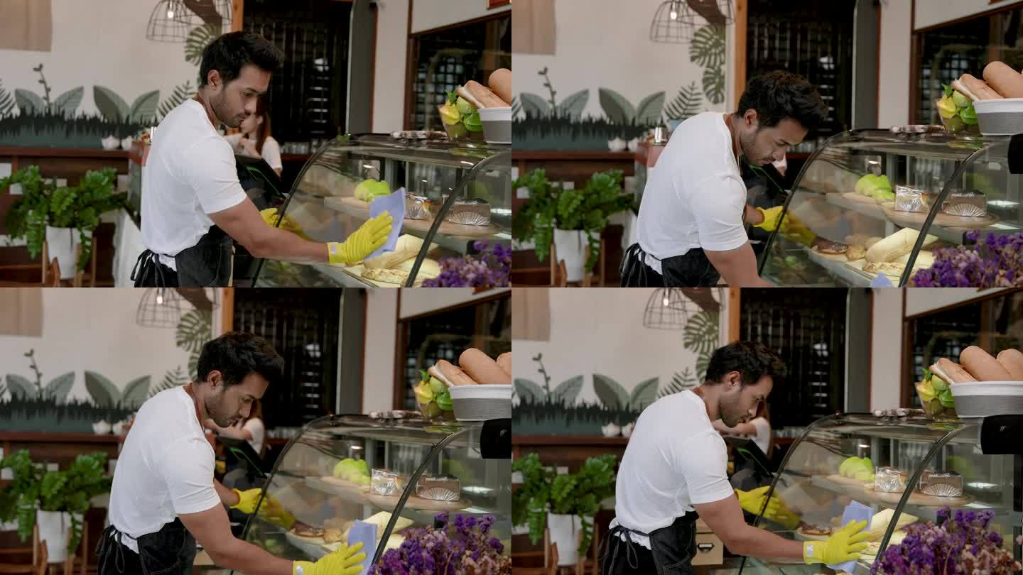 一名印度男子经营着一家小型家庭咖啡店。帮妻子清洗放蛋糕的玻璃柜。准备好每天早上开门营业。随时准备接待