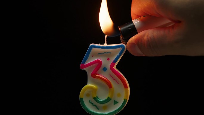 在黑色背景上用慢动作吹灭3号蜡烛的特写。三岁生日。