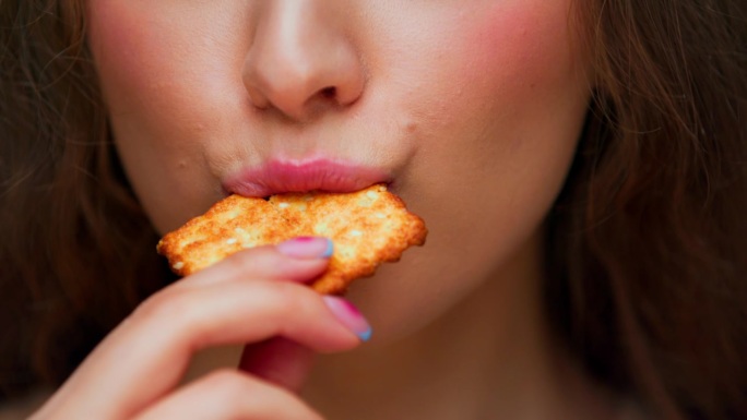 年轻女子吃甜食的特写镜头肖像。现代人在嘴里咬着松脆的芝麻饼干的短发脸。孤独饥饿女士的正常食欲与脆皮点