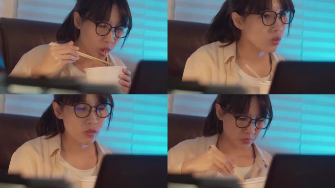 一位年轻的女商人一边在家用笔记本电脑工作一边吃方便面的4k视频片段。晚上加班