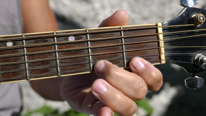 吉他手臂，指板特写镜头。有人在户外弹吉他。弹原声吉他的人。在阳光下练习吉他的人。播放音乐。拨动原声吉