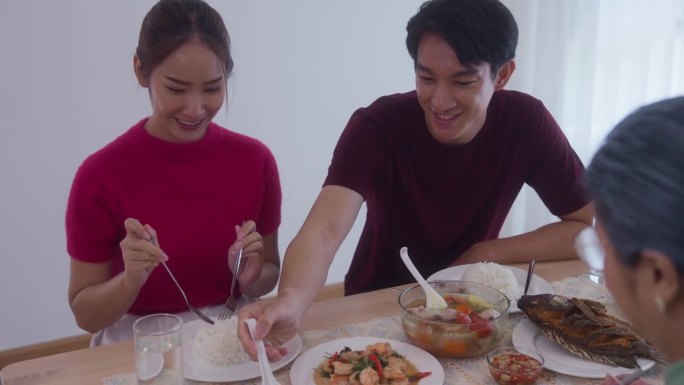 由母亲组成的亚洲家庭。儿子和儿媳正在家里吃饭，把食物放在桌子上。