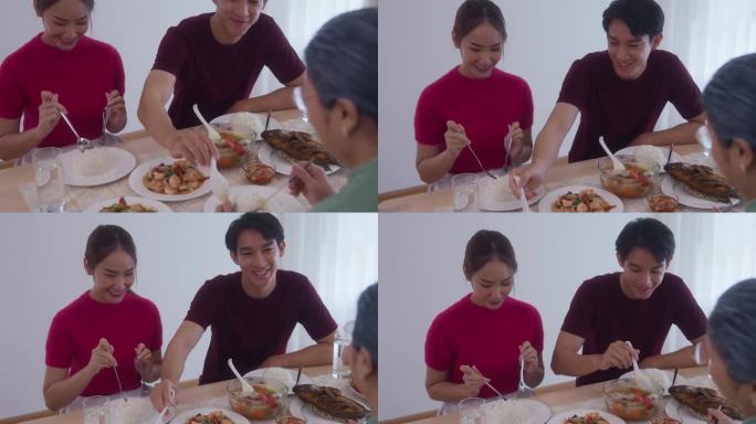 由母亲组成的亚洲家庭。儿子和儿媳正在家里吃饭，把食物放在桌子上。