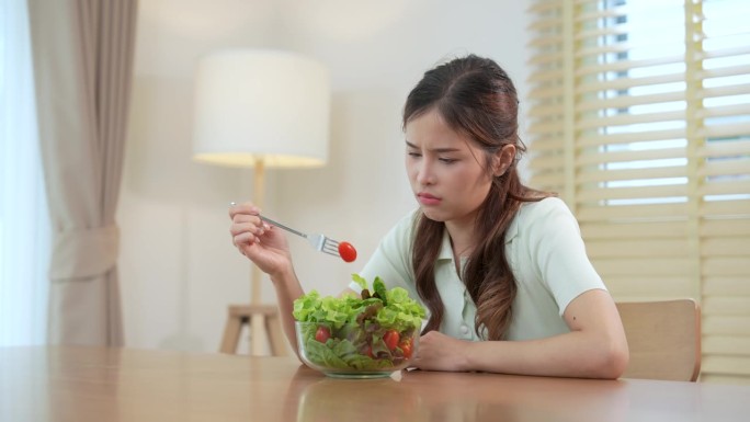 不快乐的女人无聊地看着面前的一碗有机蔬菜沙拉，因为她不喜欢吃蔬菜。