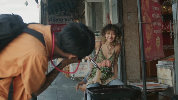 一名亚洲男子在老城区旅行时，用相机拍下了正在烤食物的女友。