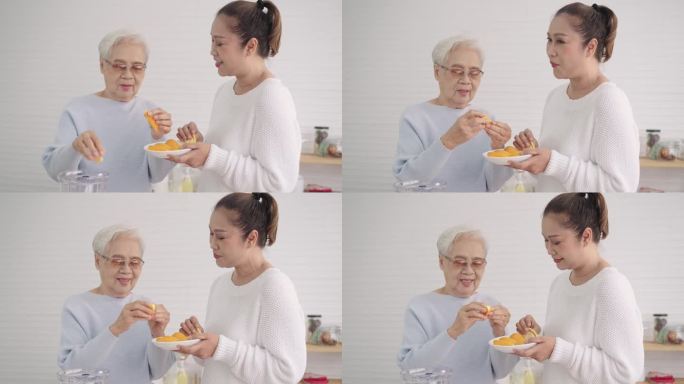 一位年长的亚洲妇女和中年的女儿在厨房里吃桔子。幸福的夫妇从橙子中摄取维生素C，在假期中使健康免于感染