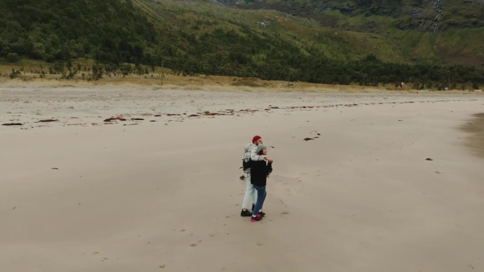 无人机拍摄了一对年轻的高加索夫妇在挪威厄斯峡湾海滩边散步，拥抱在一起