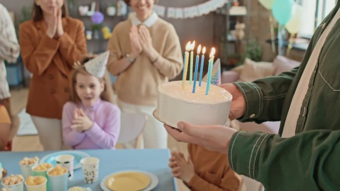 在孩子们的聚会上，父母拿着生日蛋糕和蜡烛