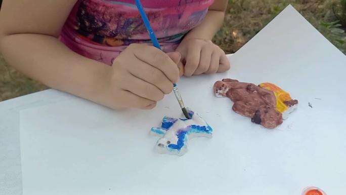 一名女小学生正在用颜料画石膏玩具。小孩的手特写。发展创新能力，精细运动技能。夏天。户外