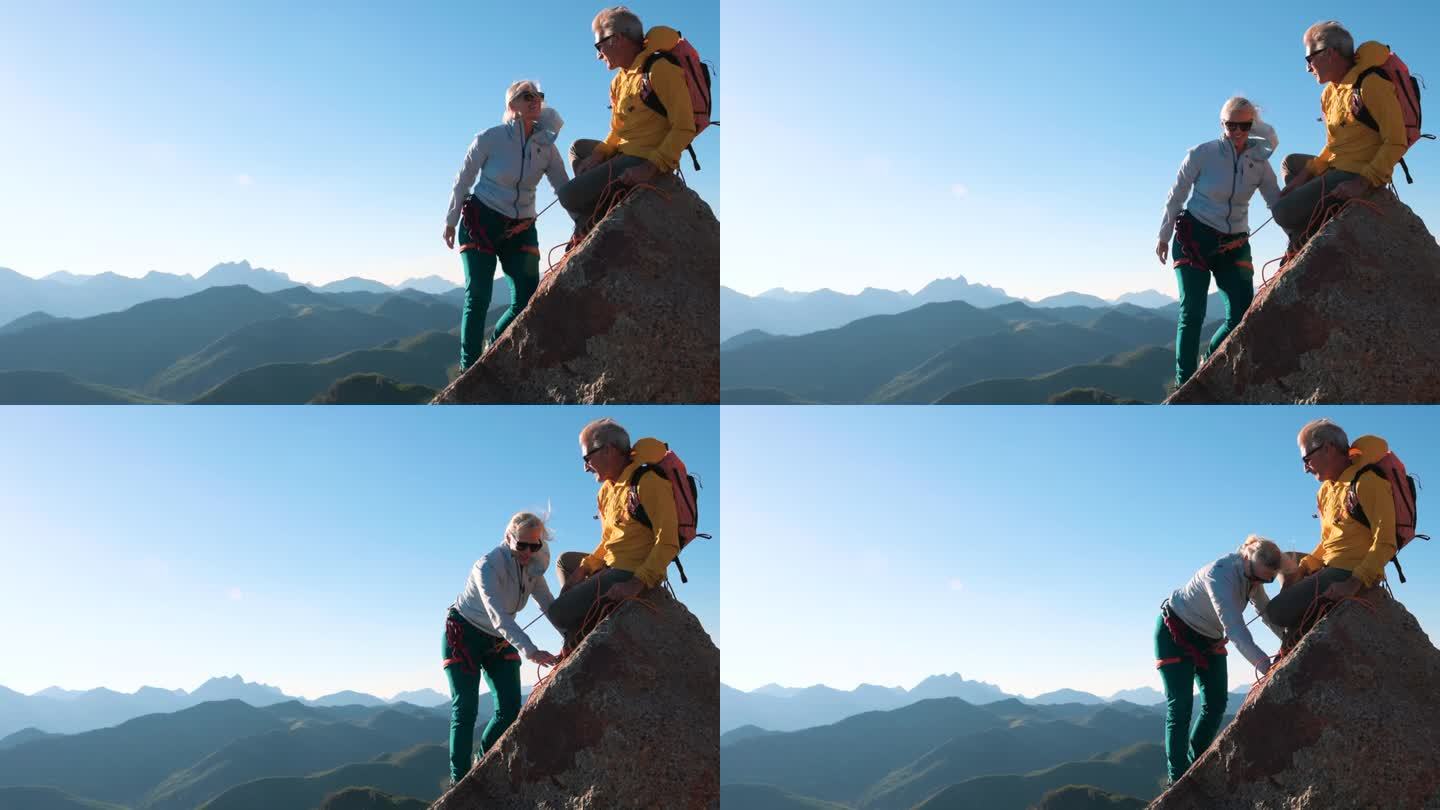 成熟的夫妇爬上山顶的岩石板
