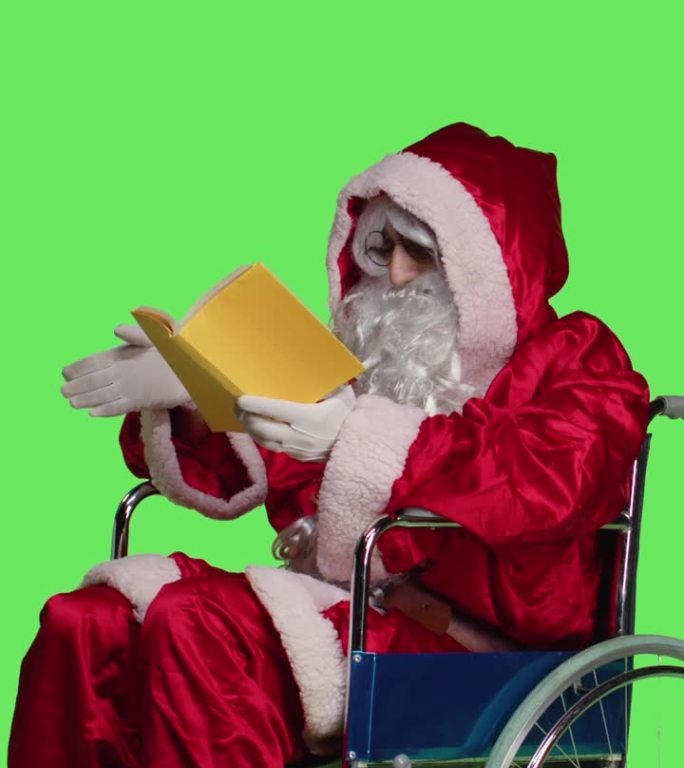 垂直视频圣诞老人坐在轮椅上看书的侧视图