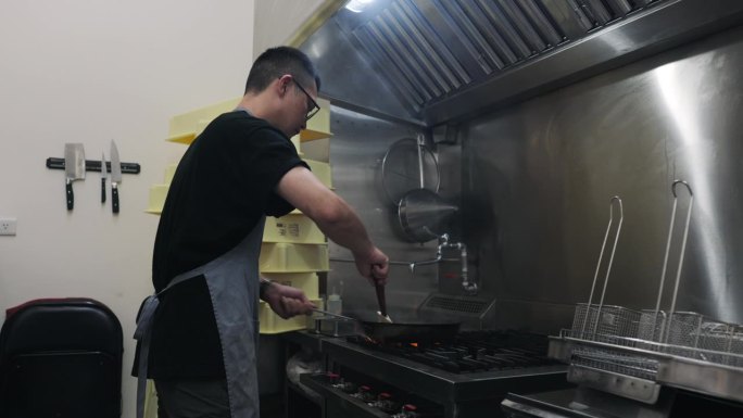 一位亚洲男性餐厅老板在开业前仔细准备食材。在厨房里，他用炒锅炒蔬菜。