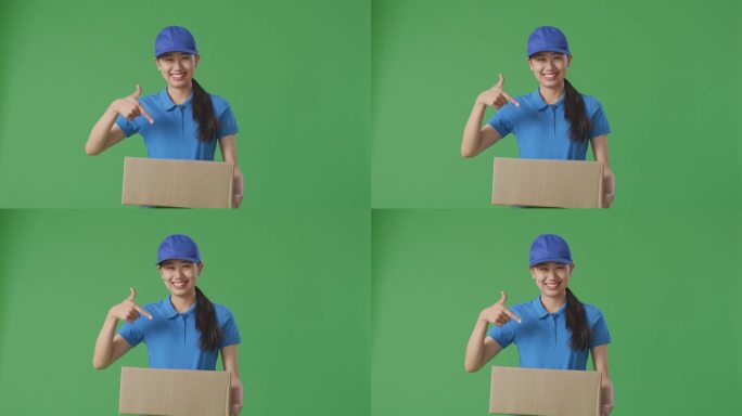 蓝色制服的亚洲女快递员微笑着指着手里的纸盒，在绿屏背景下投递