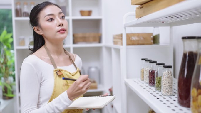 一个亚洲女人在厨房里检查家里笔记本上的购物清单。医疗保健的概念。饮食概念中的有机新鲜水果和蔬菜，在去