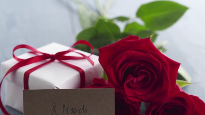 三朵红玫瑰与礼盒和纸卡与3月8日短语在蓝色木桌盘
