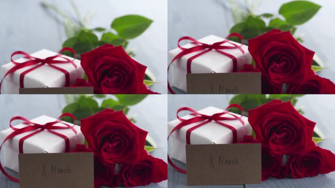 三朵红玫瑰与礼盒和纸卡与3月8日短语在蓝色木桌盘