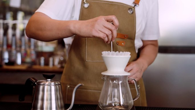 与咖啡师一起设置滴滤咖啡机，咖啡师在咖啡馆里用锋利的工具将一些滴滤咖啡抖掉，使其不会聚集在一起，以便