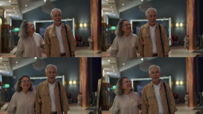 一对老年夫妇手挽着手走在走进电影院的路上，边走边聊天。