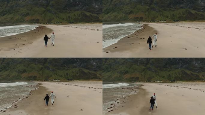无人机跟随一对无忧无虑幸福的年轻夫妇，手牵着手在挪威海边奔跑