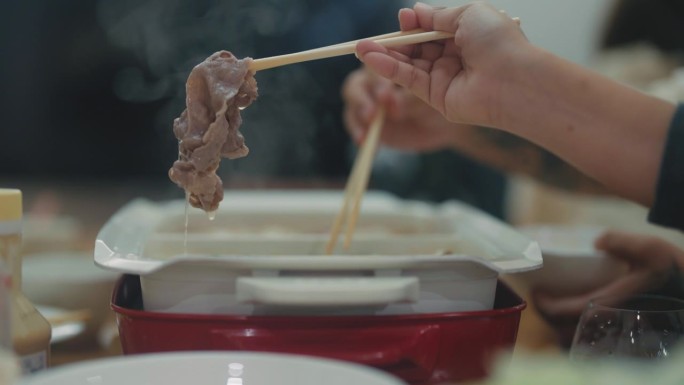 近距离的手蘸肉片在沸腾的汤锅里用筷子搅拌，日式涮锅和寿喜烧