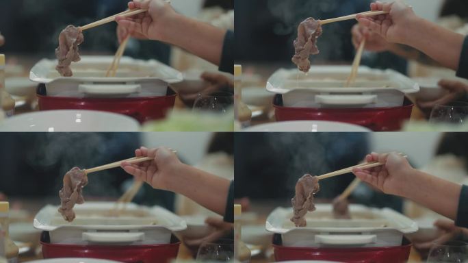 近距离的手蘸肉片在沸腾的汤锅里用筷子搅拌，日式涮锅和寿喜烧