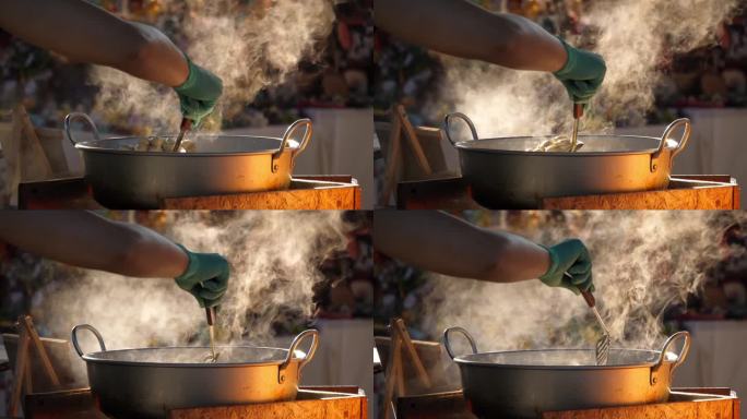 慢动作速度特写镜头，人的手用勺子搅拌锅，锅里有热油和热蒸汽流煎肉丸，街头小吃厨师在乡村摊位上烹饪。