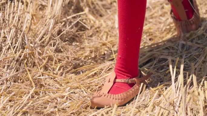穿着民族传统皮鞋的保加利亚女孩走在收割后的麦田里