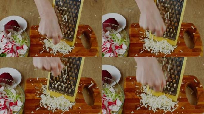 女士正在准备新鲜的蔬菜沙拉。特写:用铁制刨丝器磨芹菜根，用来做新鲜蔬菜沙拉。美味的蔬菜沙拉对健康有益
