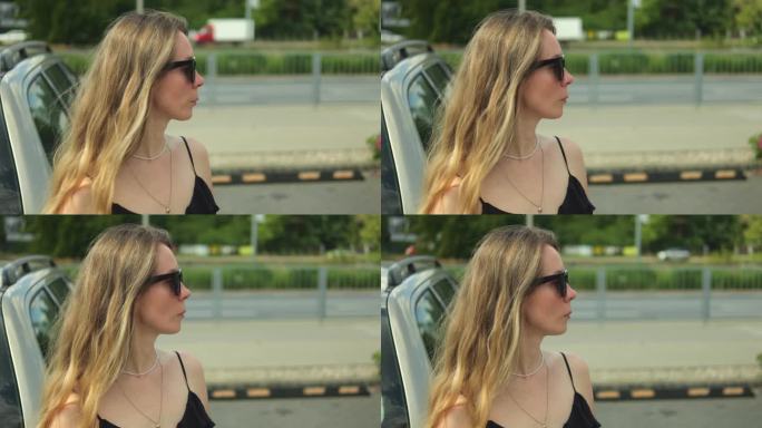 年轻优雅的女子戴着太阳镜和太阳裙在户外望向远方。在温暖的夏日里，美丽的女性变焦者站在停着的汽车旁。
