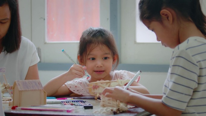 一个亚洲女孩和她的姐姐正在给一个木制玩具上色