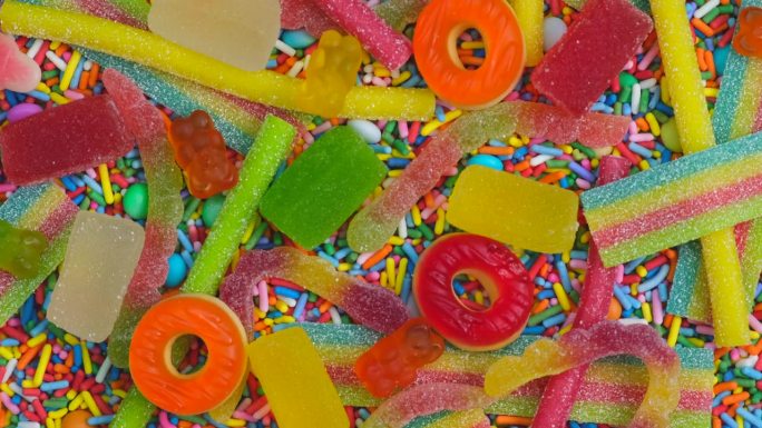 旋转背景的各种果冻糖果，熊，甜甜圈，糖果，糖果，糖霜，近距离俯瞰概念生日聚会或庆祝活动