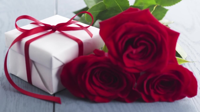 三朵红玫瑰和礼盒放在蓝色的木桌焦点拉