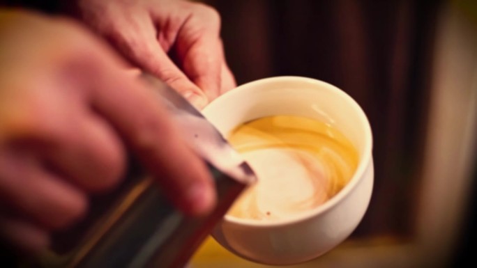 精品咖啡店里的咖啡师在做拉花。专业男士用浓缩咖啡倒流牛奶。咖啡师制作心形的咖啡拉花艺术