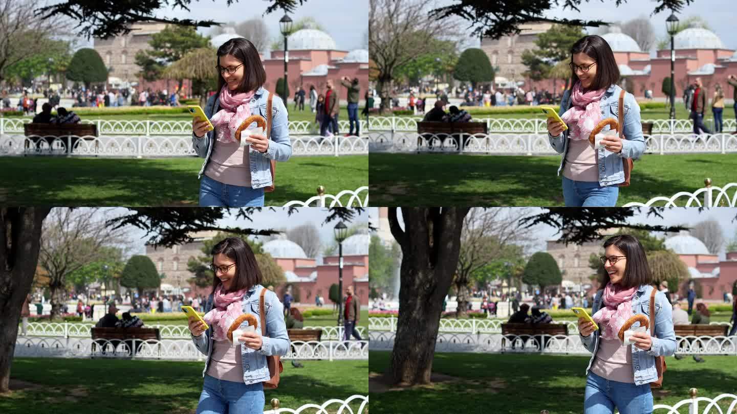 伊斯坦布尔圣索菲亚大教堂前，一名年轻女子边吃土耳其百吉饼边玩手机