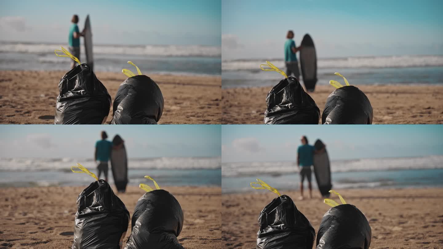 两个垃圾袋站在沙滩上，冲浪者站在水边作为背景