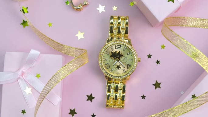 旋转背景不同的时尚女性配件，手表和礼品盒与金色丝带在粉红色的背景特写顶视图