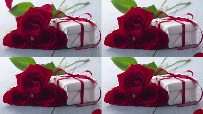 三朵红玫瑰和礼盒放在蓝色的桌子上，花瓣缓缓落下