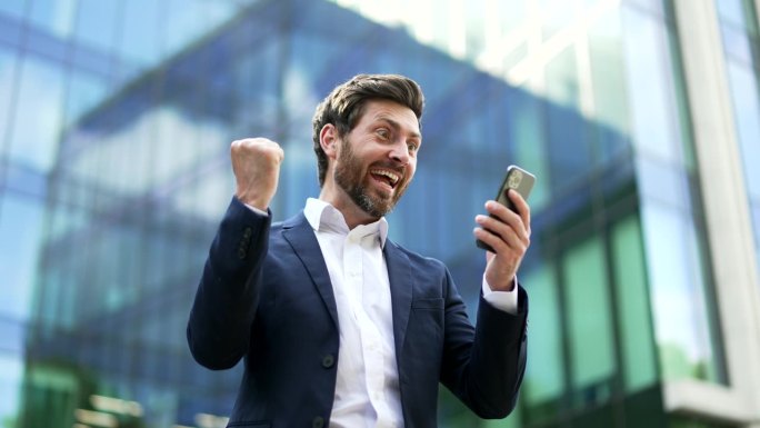 快乐的商人投资者快乐的阅读收到手机上的大好消息。