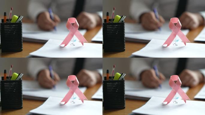 医生写字时桌上的粉红丝带乳腺癌意识标志
