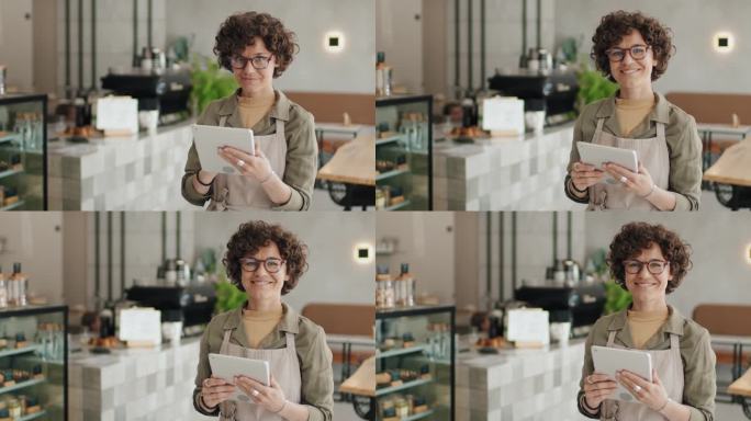 白人女服务员站在咖啡馆里，手里拿着平板电脑，面带微笑