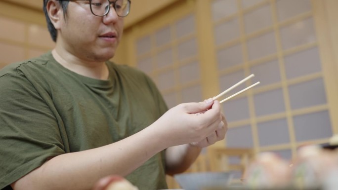 不要互相摩擦筷子。一个亚洲男人在和朋友聊天的时候把筷子掰开摩擦在一起，然后伸手去拿三文鱼寿司，一边吃