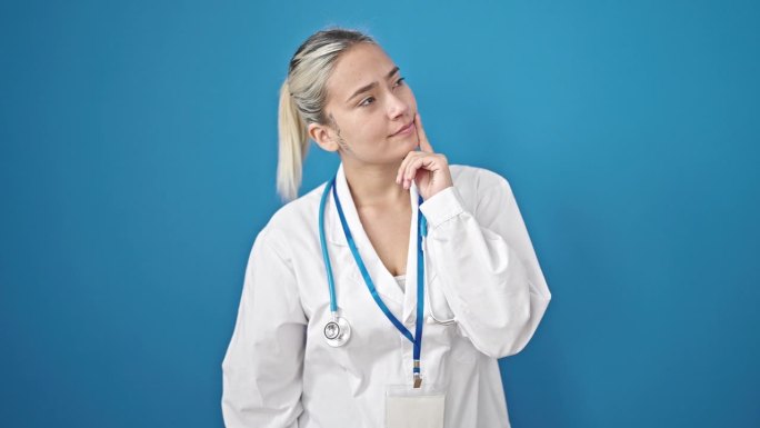 年轻美丽的西班牙女医生带着疑惑的表情站在孤立的蓝色背景上思考
