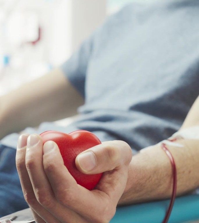 竖屏:男性献血者的手部特写镜头。男性挤压心形红球帮助泵血。需要输血的病人的捐献。