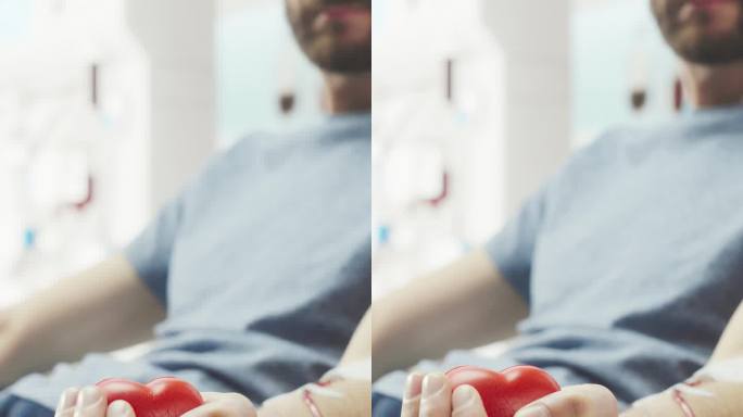 竖屏:男性献血者的手部特写镜头。男性挤压心形红球帮助泵血。需要输血的病人的捐献。