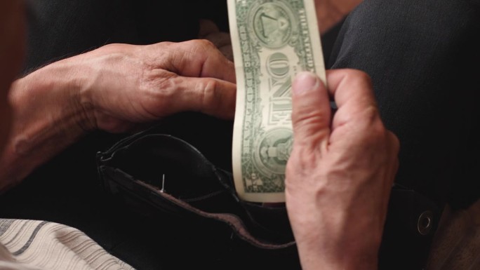 一位老人打开一个空的旧钱包，里面只有1美元。家庭预算，老年破产，金融危机，失业