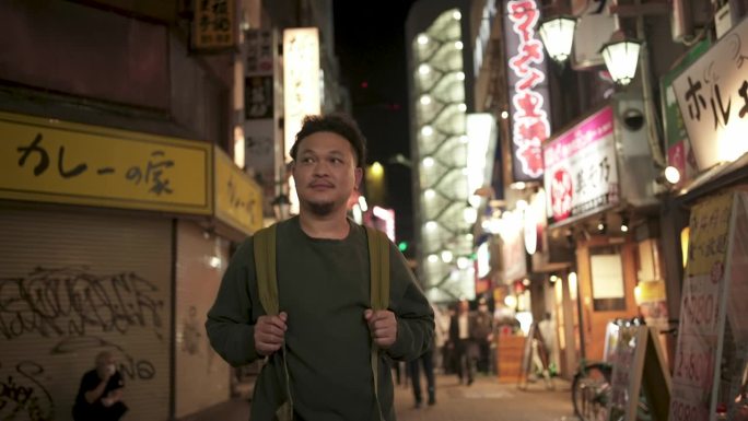 快乐的亚洲背包客在东京的街头夜市散步和环顾四周。放松,享受。他微笑着，看起来很开心